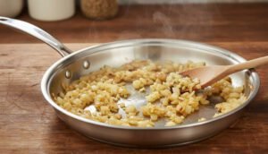 Sofrito de ajo y cebolla cocinándose de forma pareja en sartén de acero quirúrgico